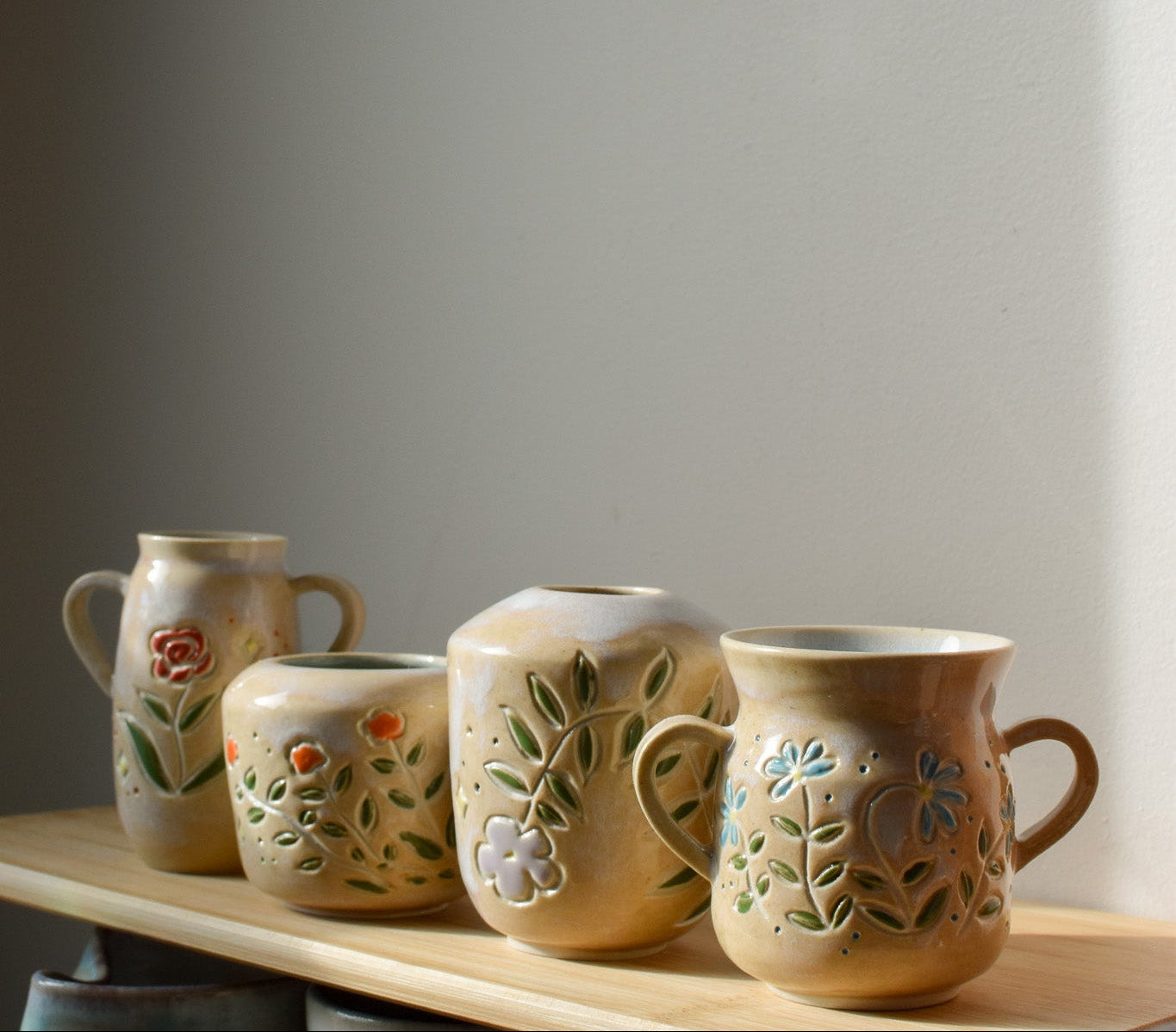 Set of ceramic mugs with floral designs on a wooden surface against a plain wall.